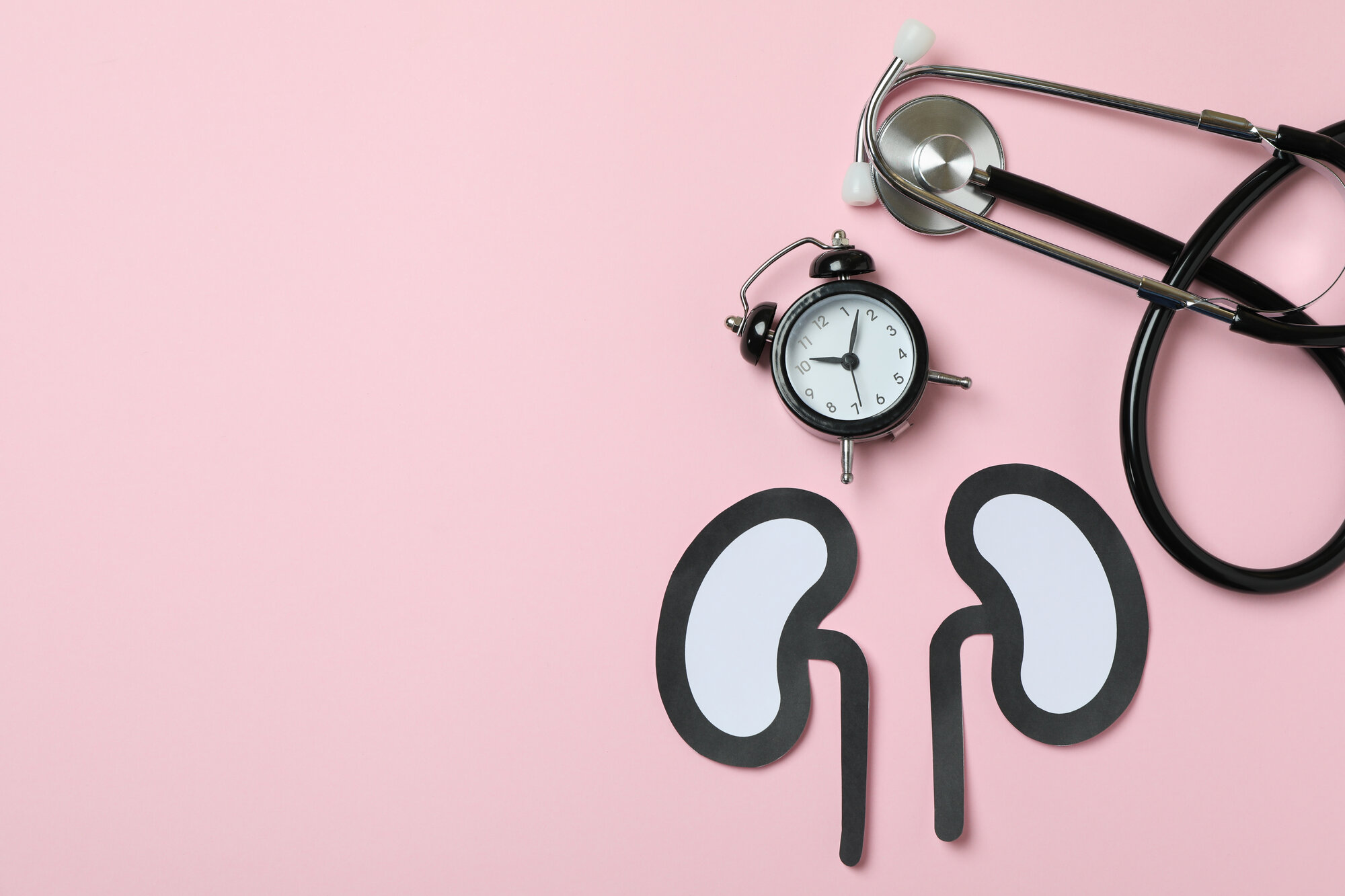 nieren gesundheit.jpg Papierfiguren von Nieren auf einem rosa Hintergrund, daneben eine Armbanduhr und ein Stethoskop.