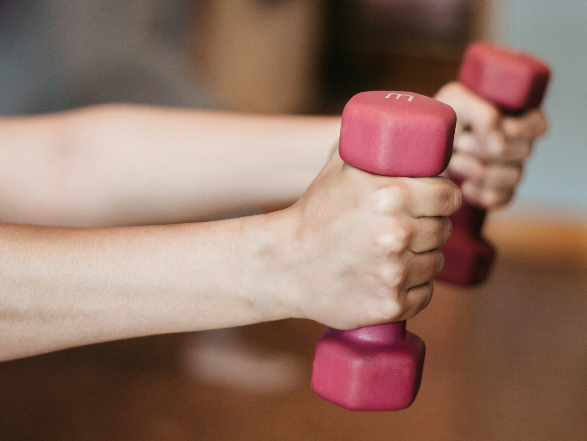 mobility training.png Hände halten zwei pinkfarbene Kurzhanteln in einem Fitnessstudio.