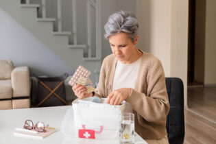 medikamente lagerung.jpeg Eine Frau in einem hellen Raum untersucht einen durchsichtigen Medikamentenbehälter und hält eine Packung Tabletten.