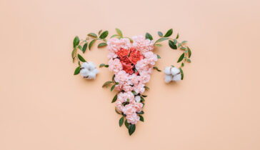 vaginaleGesundheit.jpeg Ein florales Arrangement in Herzform aus rosa Blumen und Baumwollblüten auf einem pfirsichfarbenen Hintergrund.