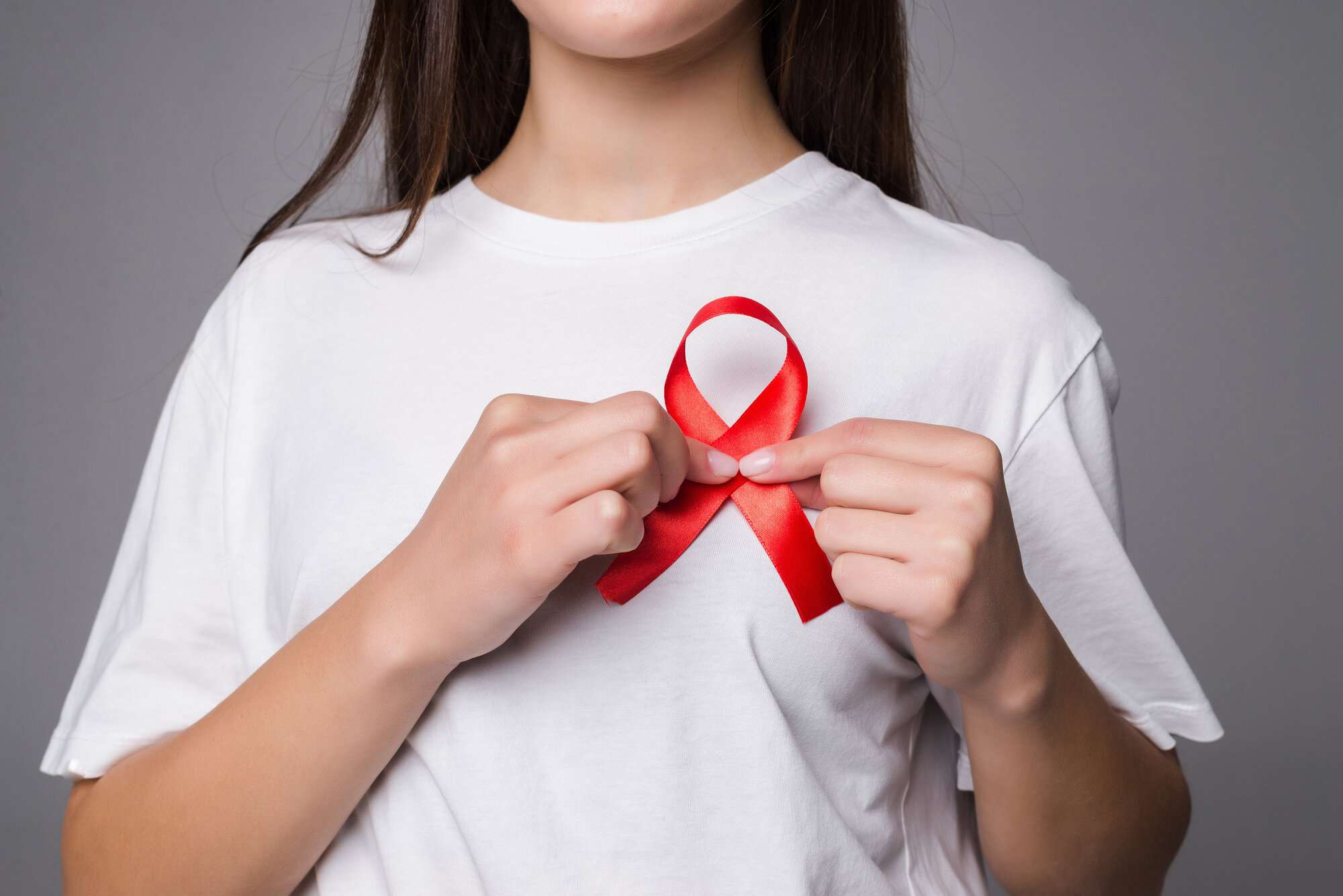 woman holding breast with pink ribbon white wall concept photo support breast cancer cause ps you can change pink ribbon into red aids support cause.jpg
